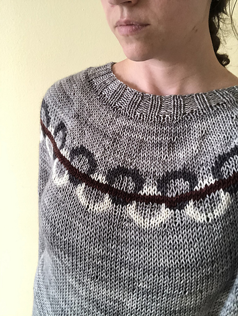 A grey pullover yoke sweater. The yoke is decorated with black and white linked circles and a burgundy line running horizontally across the links.