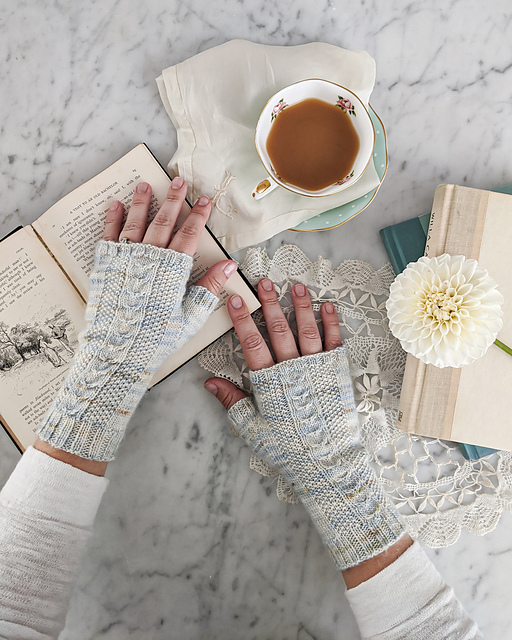 Fingerless mitts knit with columns of cables between sections of seed stitch, with a ribbed brim, knit in pale grey, pale blue and tan variegated yarn.