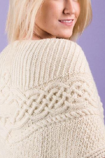 A blond woman modelling a cream shawl with large celtic braid cable motif running horizontally across it