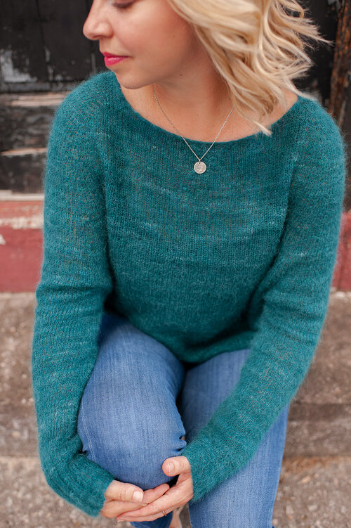 A blonde woman modelling a knit raglan pullover with crew neck and long sleeves, in tonal teal yarn