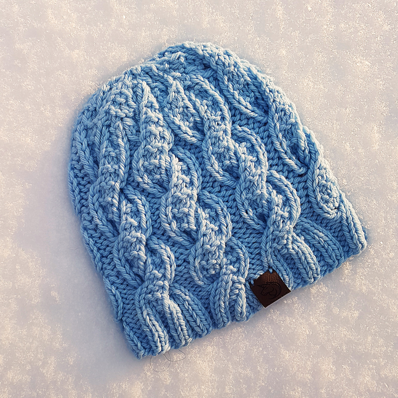 A pale blue, bulky cabled knit hat, on a bed of fresh snow.