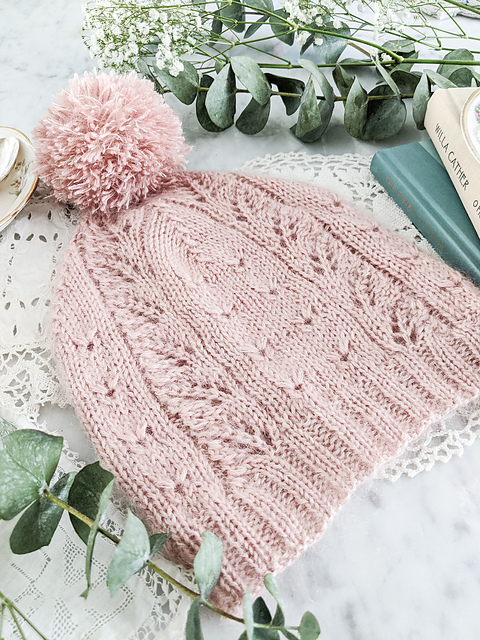 A soft pink lace knit hat with matching pom pom
