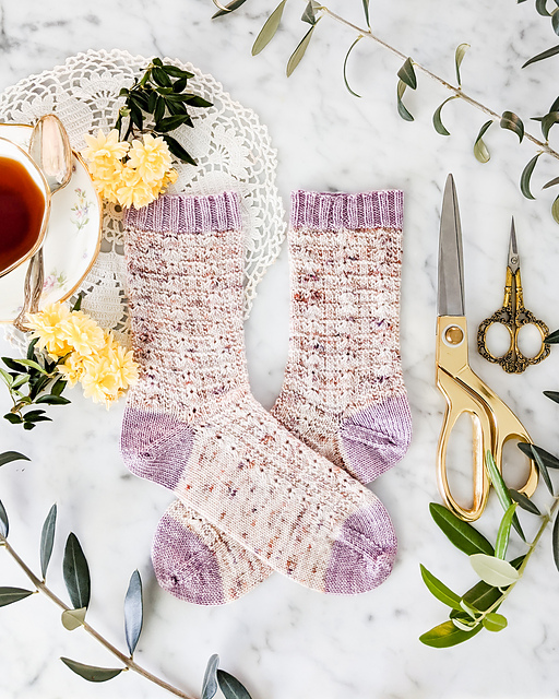 Textured socks knit in pink speckled yarn with lilac contrasting toe, cuff, and heel.