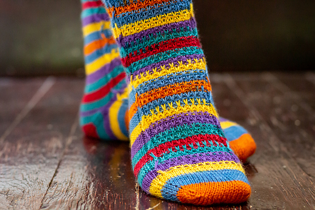 Vibrant blue, orange, yellow, purple, teal, and red socks with a textured slip stitch pattern on the instep.