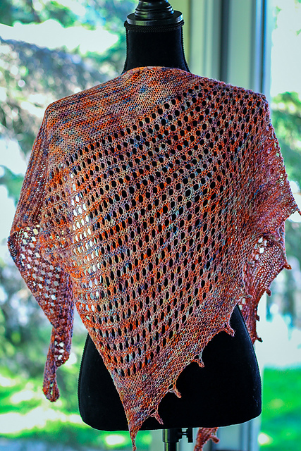 A mesh and garter triangle shawl knit in orange, red, and blue variegated yarn with a picot edge