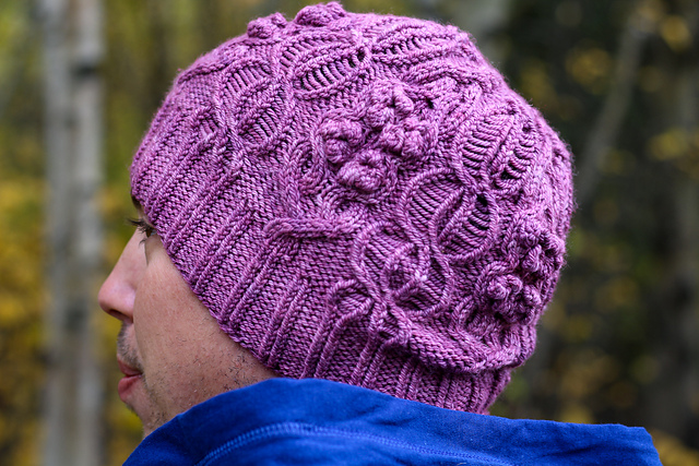 A magenta knit hat with cables, bobbles, and dropped stitches