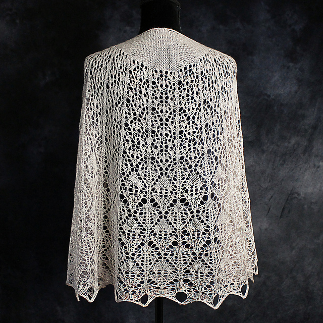 A cream crescent shawl with elegant allover lace, displayed on a dress form.