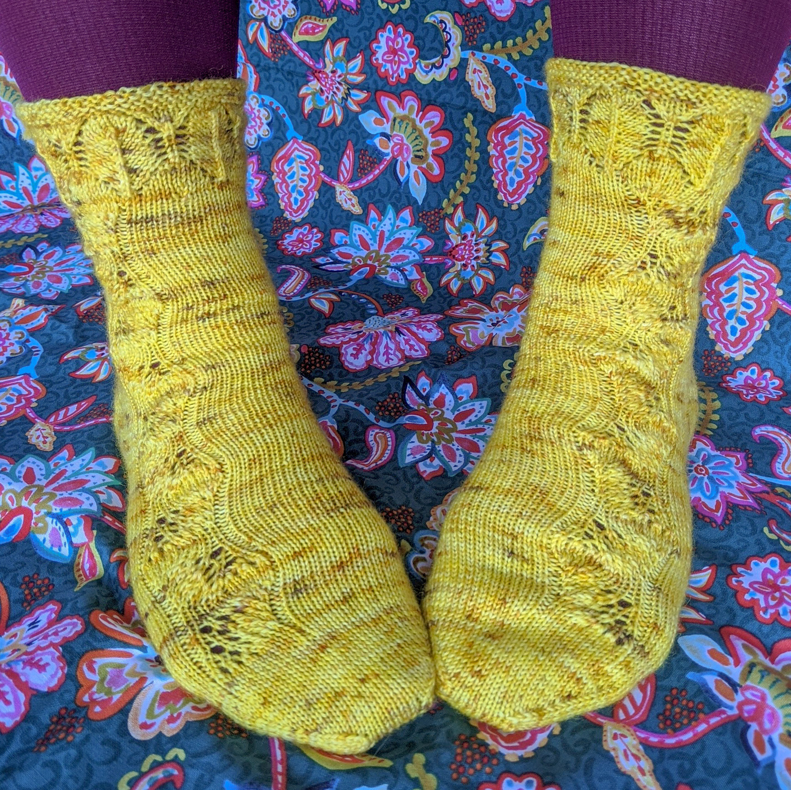 A yellow speckled sock with feather lace encircling the cuff and continuing in a single column along the instep.
