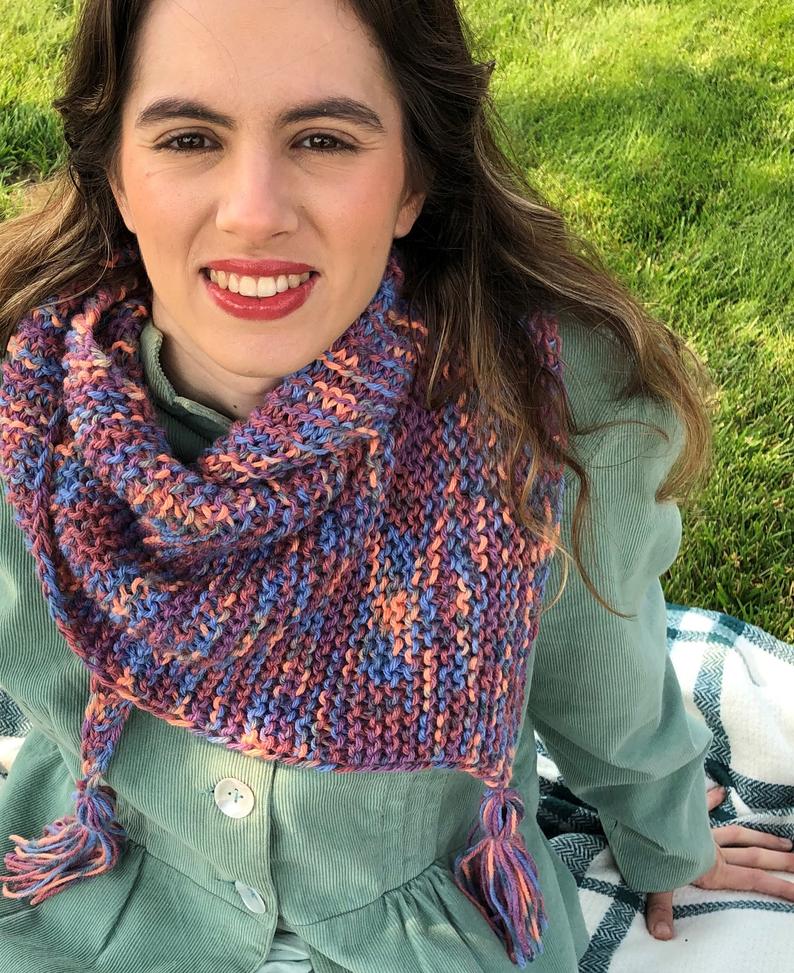 A smiling young woman with a purple and pink variegated garter triangle shawl around her neck