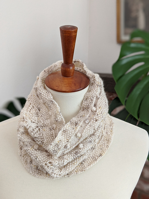 A seed stitch, lace, and bobble cowl, knit in cream yarn with brown speckles