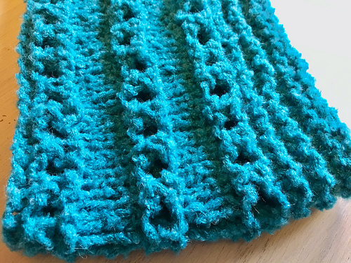 Cowl in a chunky textured yarn with rows of pronounced eyelets contrasting with rows of stockinette.